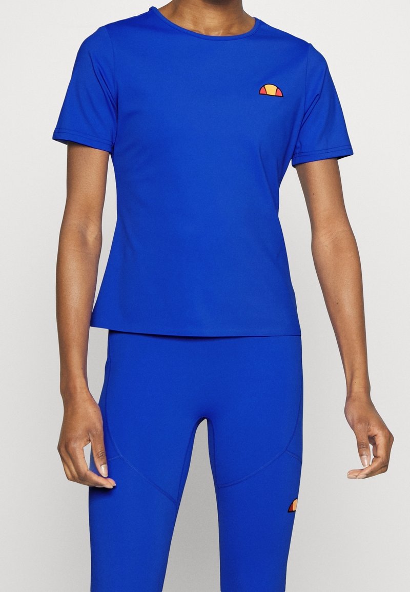 Personne portant un haut bleu à manches courtes ajusté et des leggings bleus assortis avec un petit logo orange et rouge sur les deux.