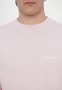 Helle rosa Baumwoll-T-Shirt mit Rundhalsausschnitt und kurzen Ärmeln, mit dem weißen Schriftzug "No Problemo" auf der Brust.