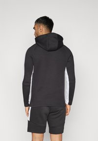 Zwarte hoodie met een capuchon, voorzien van witte zijstrepen en een getailleerd ontwerp. Gecombineerd met bijpassende zwarte shorts voor een samenhangende look.
