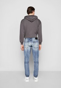 Sweat à capuche gris court, associé à un jean skinny déchiré bleu clair. Le mannequin porte des baskets blanches avec des accents noirs.