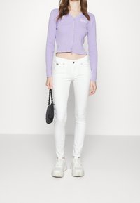 Cárdigan de rayas moradas con escote en V y botones, combinado con jeans skinny blancos, zapatillas blancas y un pequeño bolso negro.