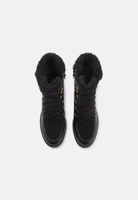 Bottes noires à lacets présentant un dessus en peluche, un bas en cuir lisse, des accents en métal et un design de pointe arrondie. Fini chaud et texturé.