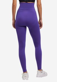 Leggings viola a vita alta con pannelli testurizzati, design aderente e finitura liscia, abbinati a scarpe da ginnastica bianche.