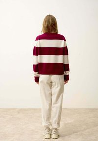Pull rayé aux couleurs bordeaux et blanc, texture tricotée, épaules tombantes, associé à un pantalon en velours côtelé crème et des baskets beiges.