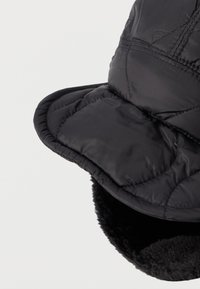 Pălărie izolată de culoare neagră, cu un design matlasat, cu o margine frontală îndreptată în jos și o căptușeală interioară pufoasă pentru căldură. Prezintă accente de cusături.