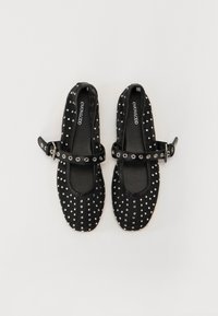Ballerines noires en toile avec un bout arrondi, dotées d'une sangle avec des accents cloutés et d'une texture lisse. L'intérieur possède une semelle rembourrée.