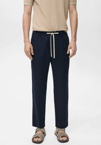 Marineblauwe broek met een ruime pasvorm, voorzien van een beige trekkoord in de taille. De stof oogt lichtgewicht en heeft een gladde textuur.