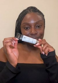 L'Oréal Prime Lab 24H Emitter, un tube de compression noir et blanc avec des accents argentés, tenu par une personne portant un haut noir, présentant une texture lisse.
