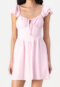 Rosa ärmlös klänning med en samlad bodice, volangaxelband och en knytfront. Urtavla i utsvängd stil med slät textur.