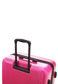 Pink hard-shell suitcase with a black retractable handle and zipper. Features a textured grip on the handle and side wheels for portability.