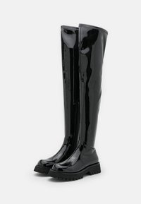 Botas de goma negras hasta la rodilla, brillantes, con suela de tracción robusta y cremallera lateral, que presentan un acabado suave y brillante y un diseño de puntera redondeada.
