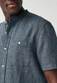 Camicia a maniche corte con colletto, in tessuto blu scuro dalla trama a quadri, con taschino sul petto e bottoni di colore chiaro.