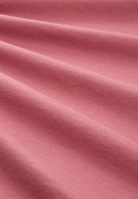 Lichtroze katoenen stof met een gladde textuur, voorzien van subtiele plooien en kreukjes, met een zachte, matte afwerking.