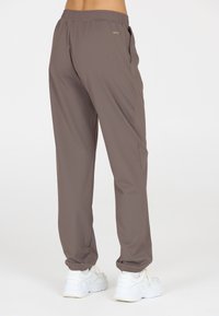 Leichte, dehnbare braune Jogginghosen mit einem elastischen Bund, seitlichen Taschen und schmal zulaufenden Bündchen, kombiniert mit weißen Sportschuhen.