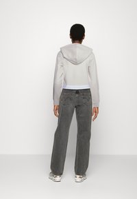 Zkrácená šedá mikina s kapucí a bílým pruhem, spárovaná s volně střiženými šedými džíny s prošíváním na zadních kapsách a teniskami.