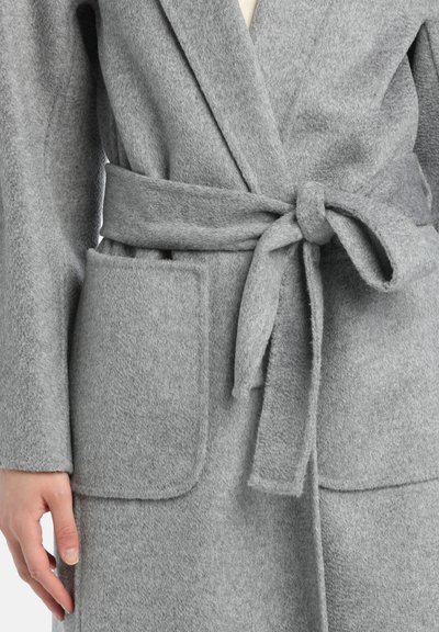 Cappotto lungo grigio in misto lana con cintura legata in vita e due grandi tasche frontali. Presenta una texture morbida e un design con ampio risvolto.