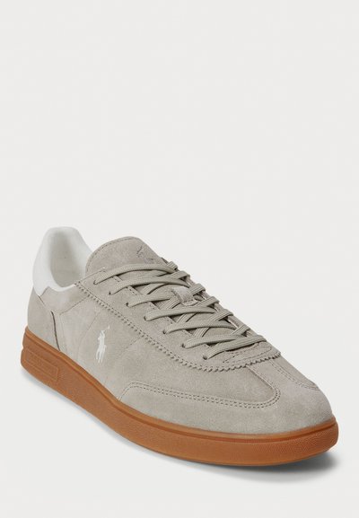 Sneaker in suede grigio con tallone in pelle bianca, lacci piatti e suola in gomma tan texturizzata. Presenta un logo ricamato sul lato.