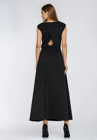 Czarna sukienka maxi z krótkimi rękawkami typu kaptur, z odkrytymi plecami i białymi groszkami. Charakteryzuje się swobodną sylwetką i została wykonana z lekkiego materiału.