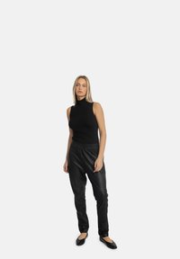 Sort ærmeløs turtleneck-top kombineret med sorte faux læder joggers, der har et elastisk taljebånd og en tapered ben-design, båret med sorte flade sko.