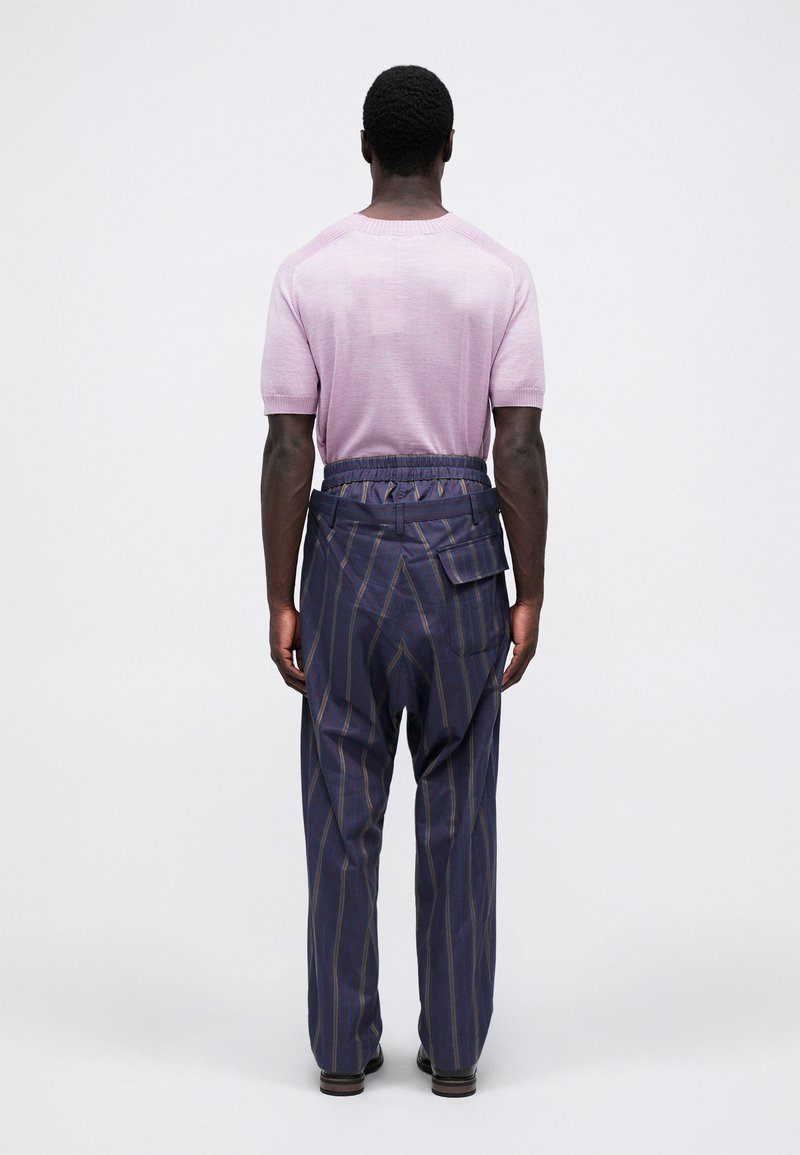 Camicia a maniche corte di maglia rosa chiaro con scollo a girocollo, abbinata a pantaloni a righe blu navy con tasche e vita elastica.