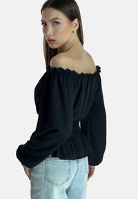 Schwarze schulterfreie Bluse mit gerafften Kanten und langen Ärmeln, mit smock-tailliertem Bund, kombiniert mit hellem Denim-Jeans.