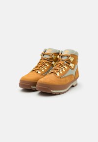 Botas de senderismo de ante marrón con acentos de nylon gris, herrajes dorados y una suela de goma resistente, que cuentan con un cuello acolchado y ojales reforzados.
