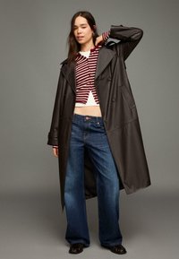 Długi czarny skórzany płaszcz typu trencz, krótkie sweter w paski w bordowo-białych kolorach, szerokie dżinsy o luźnych nogawkach, czarne buty oraz minimalistyczne detale w postaci akcesoriów.