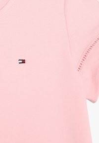 Chemise rose à manches courtes en coton doux, ornée d'un petit logo brodé en rouge, blanc et bleu sur la poitrine.