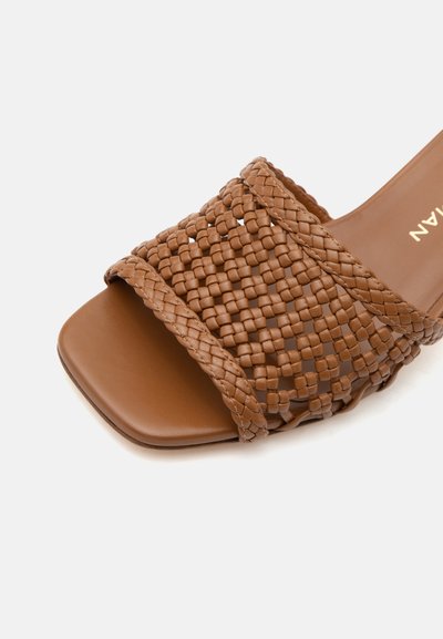 Sandale mule ouverte marron avec une large bride en cuir tressé et un design carré à l’avant sur fond blanc.