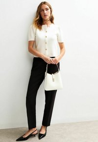 Weißes kurzärmliges, geknöpftes Oberteil, schwarze maßgeschneiderte Hose, schwarze spitze Absätze und eine weiße Schultertasche. Einfaches, elegantes Design mit goldenen Akzenten.