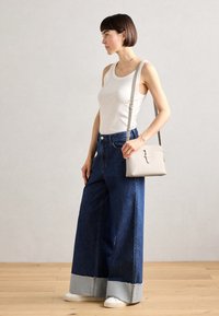 Džínové kalhoty s širokým střihem a světlemodrým lemováním, kombinované s bílým tílkem. Malá béžová crossbody kabelka se zipem a dekoračními detaily.