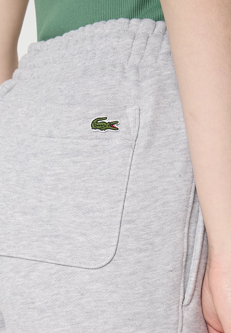 Szare bawełniane dresy z elastycznym pasem i kieszeniami bocznymi, z małym, zielonym haftowanym logo krokodyla na lewej kieszeni.