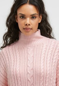 Hellrosa pullover mit Kabelstrickmuster und hohem Kragen, geprägt von einer gerippten Textur und gedrehten Mustern im gesamten Stoff.