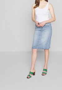 Světle modrá džínová tužková sukně s rovného střihu a ke kolenům. Kombinováno s černými a zelenými pruhovanými muly na blokovém podpatku. Bílý tílko.