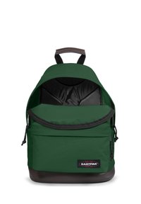 Grön tygryggsäck med en stor öppning, vadderad insida, svart foder och en strukturerad brun botten. Har en framficka med dragkedja och logotyp.