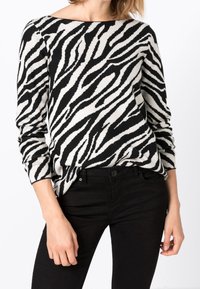 Svartvitrandig zebra-mönstrad tröja, mjukt stickat material, bred båtformad halsringning, långa ärmar, kombinerad med svarta åtsittande byxor.