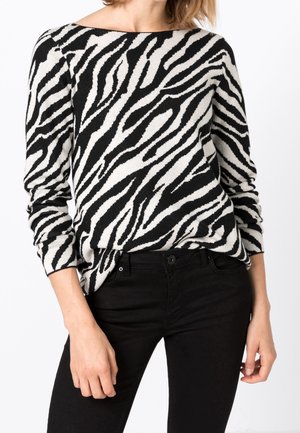 Stribet sweater i sort og hvidt med zebramønster, blødt strikmateriale, bred bådudskæring, lange ærmer, parret med tætsiddende sorte bukser.