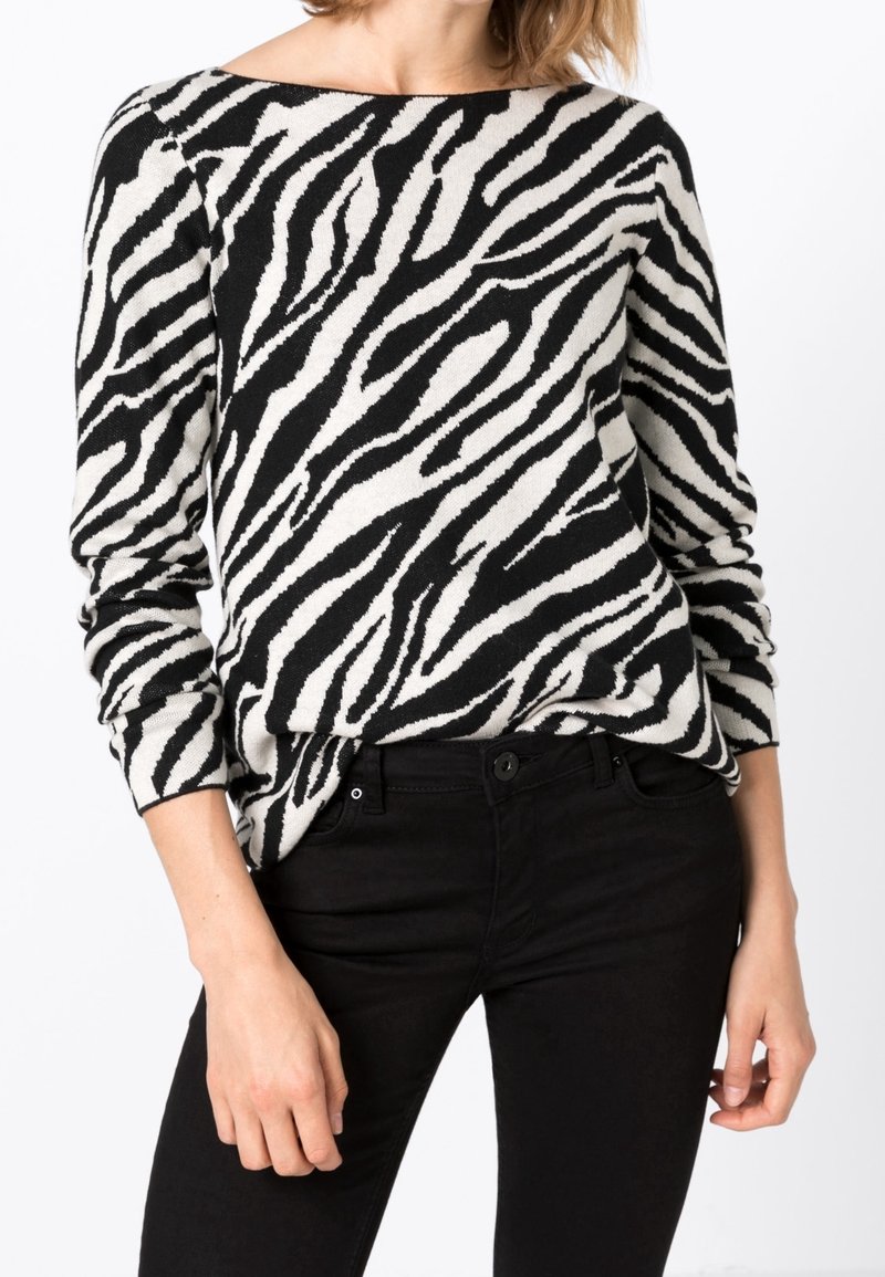 Svartvitrandig zebra-mönstrad tröja, mjukt stickat material, bred båtformad halsringning, långa ärmar, kombinerad med svarta åtsittande byxor.