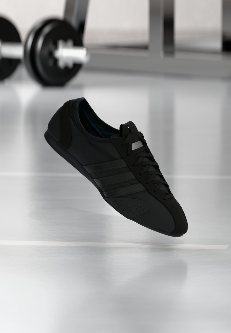 Μαύρο αθλητικό παπούτσι με αεροδυναμικό σχεδιασμό, λείο συνθετικό υλικό, κλείσιμο με κορδόνια και διακοσμητικές τρύπες στη μύτη.