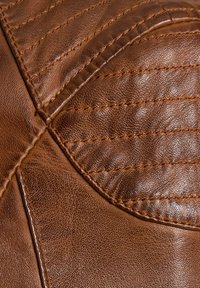 Bruin leer met gedetailleerde stiksels en gegoten, gewatteerde secties die geometrische patronen vormen.