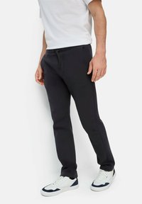 Zwarte sweatpants met een trekkoord in de taille, zijzakken en een taps toelopende pasvorm, gecombineerd met witte sneakers met marineblauwe accenten.