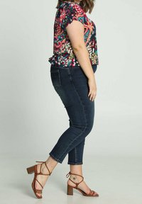 Blusa floral colorida con mangas cortas, combinada con jeans skinny de color azul oscuro y sandalias de tacón estriado marrón con tacón cuadrado.