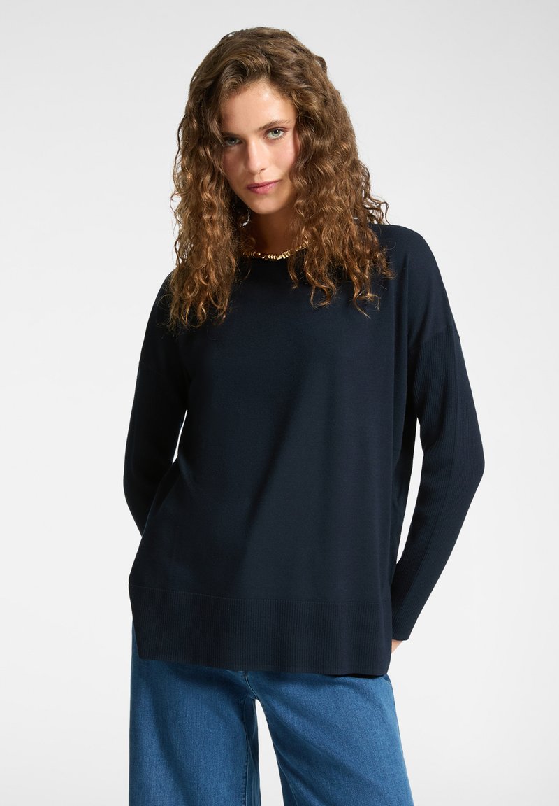 Maglione a maglia blu navy con polsini e orlo a coste, caratterizzato da una vestibilità rilassata e un colletto rotondo. Tessuto morbido, abbinato a jeans a gamba larga.