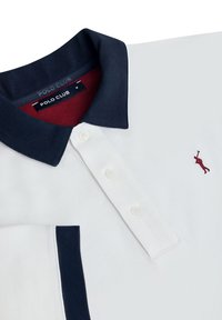 Hvid polo-shirt med en navy krave og røde accenter. Har et lille broderet logo og tre hvide knapper på placket.