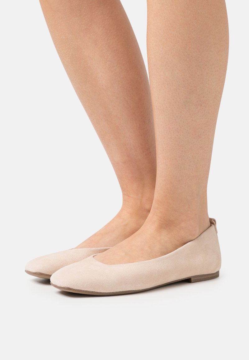 Ballerines en daim beige avec un bout arrondi et un talon bas et plat. Texture lisse avec un design minimaliste et sans matériel proéminent.