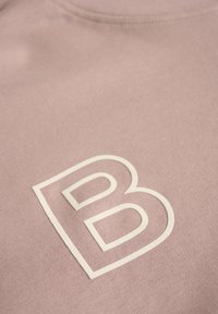 Heled roosa sviiter, millel on suur valge "B" logo. Kude on pehme ja sile ning klassikalise ümmarguse kaelusega disain.