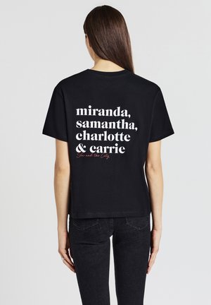 T-shirt en coton noir avec du texte blanc au dos : « miranda, samantha, charlotte & carrie » et « Sex and the City » en rouge. Coupe décontractée.