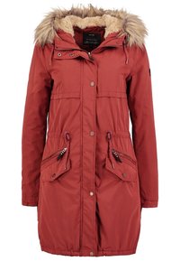 Long manteau d'hiver rouge rouille avec capuche bordée de fausse fourrure, fermeture éclair frontale, boutons pression et deux poches zippées avec rabats.
