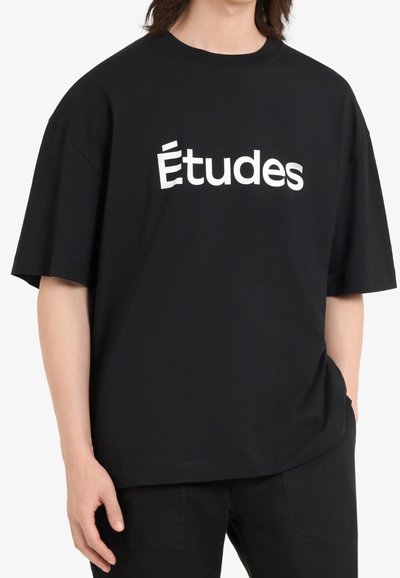 T-shirt oversize noir en coton, avec des manches courtes et un col rond, portant "Études" imprimé en grandes lettres blanches sur le devant.