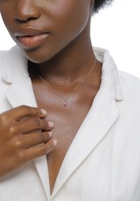Collier en argent avec un pendentif en pierre précieuse rose porté sur une peau nue, associé à une chemise blanche à col. Texture lisse et design délicat.